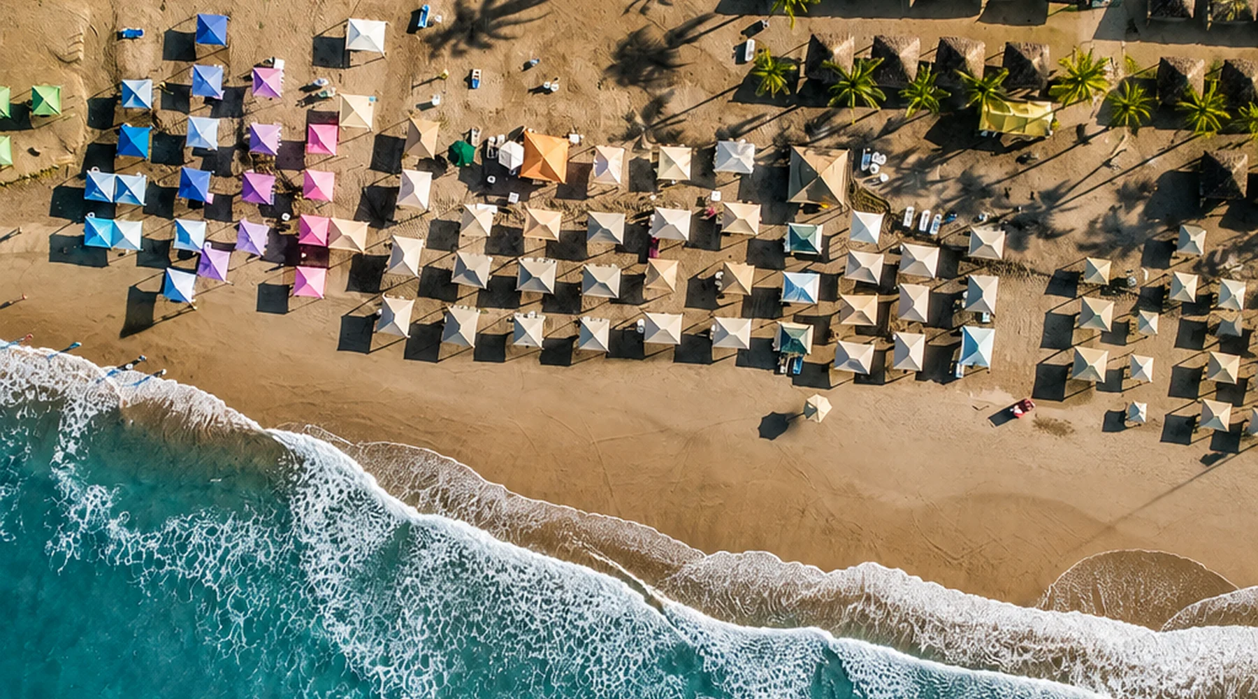 Vista aérea de una playa de Acapulco con sombrillas, palmeras y oleaje